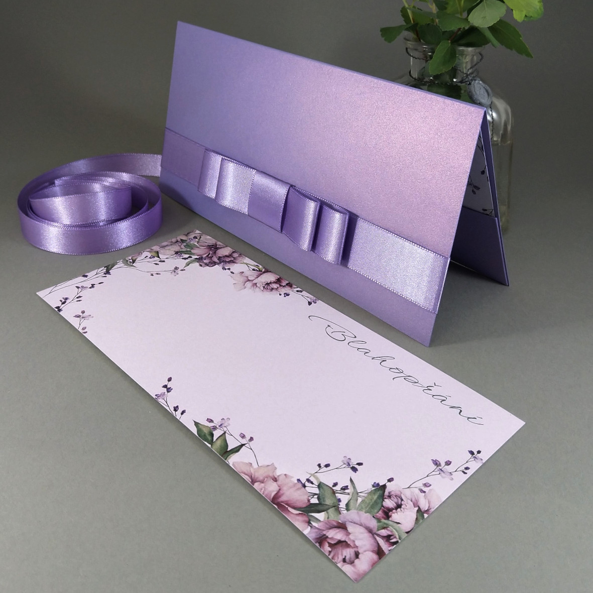 Blahopřání – jednoduchá karta s motivem pivoněk vložená do dárkové obálky, převládající barva fialová.