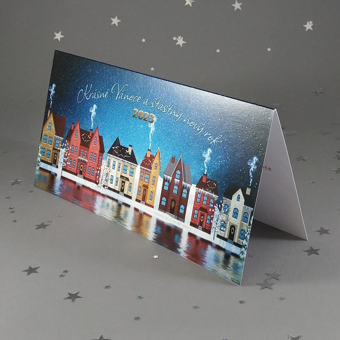 Novoroční–vánoční přání z bílého perleťového papíru s zimním motivem domků na nábřeží. Otevírací, DL formát 200 × 100 mm.