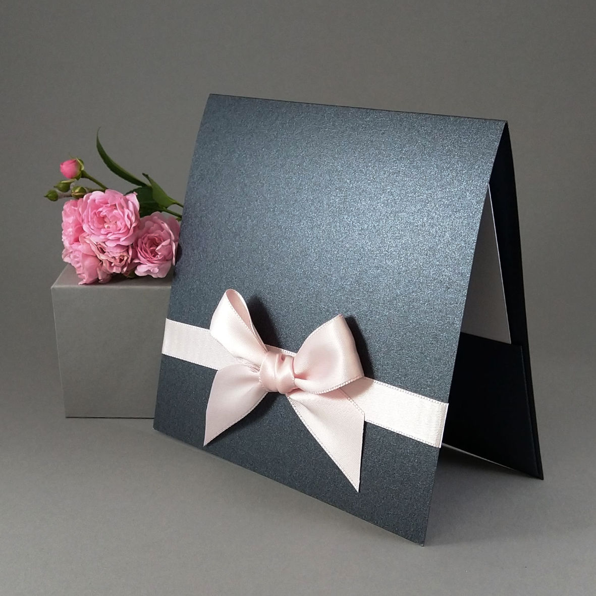 Dárková kapsa čtvercová z tmavě šedého perleťového papíru s růžovou mašlí, formát 150 × 150 mm.