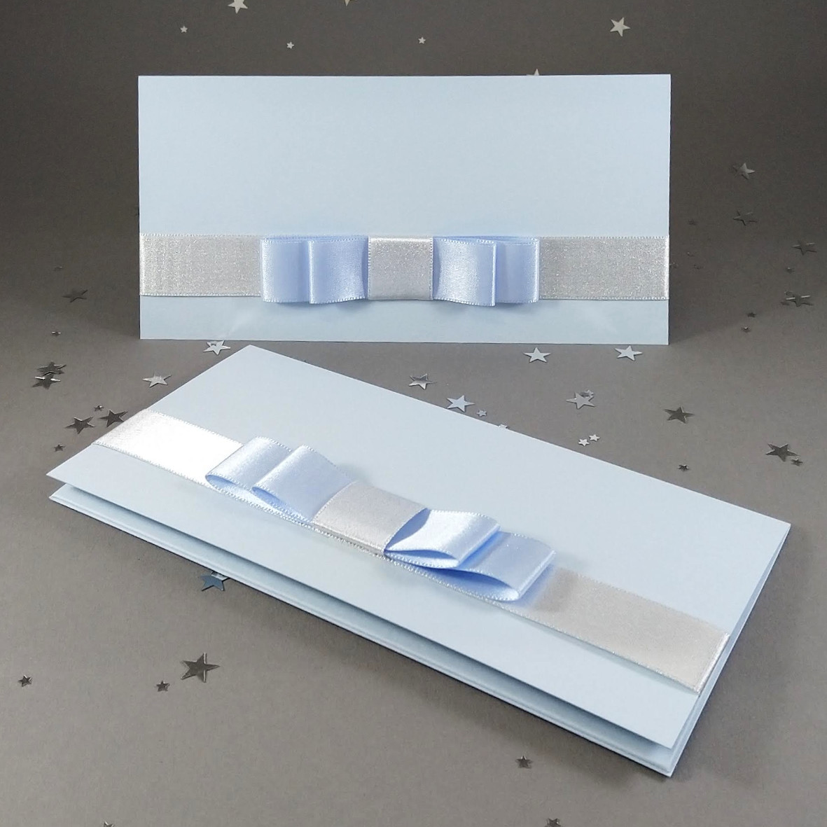 Dárková kapsa DL formátu z matného, mírně strukturovaného, světle modrého papíru, s aplikací z široké atlasové stuhy, celkový rozměr 206 × 106 mm.
