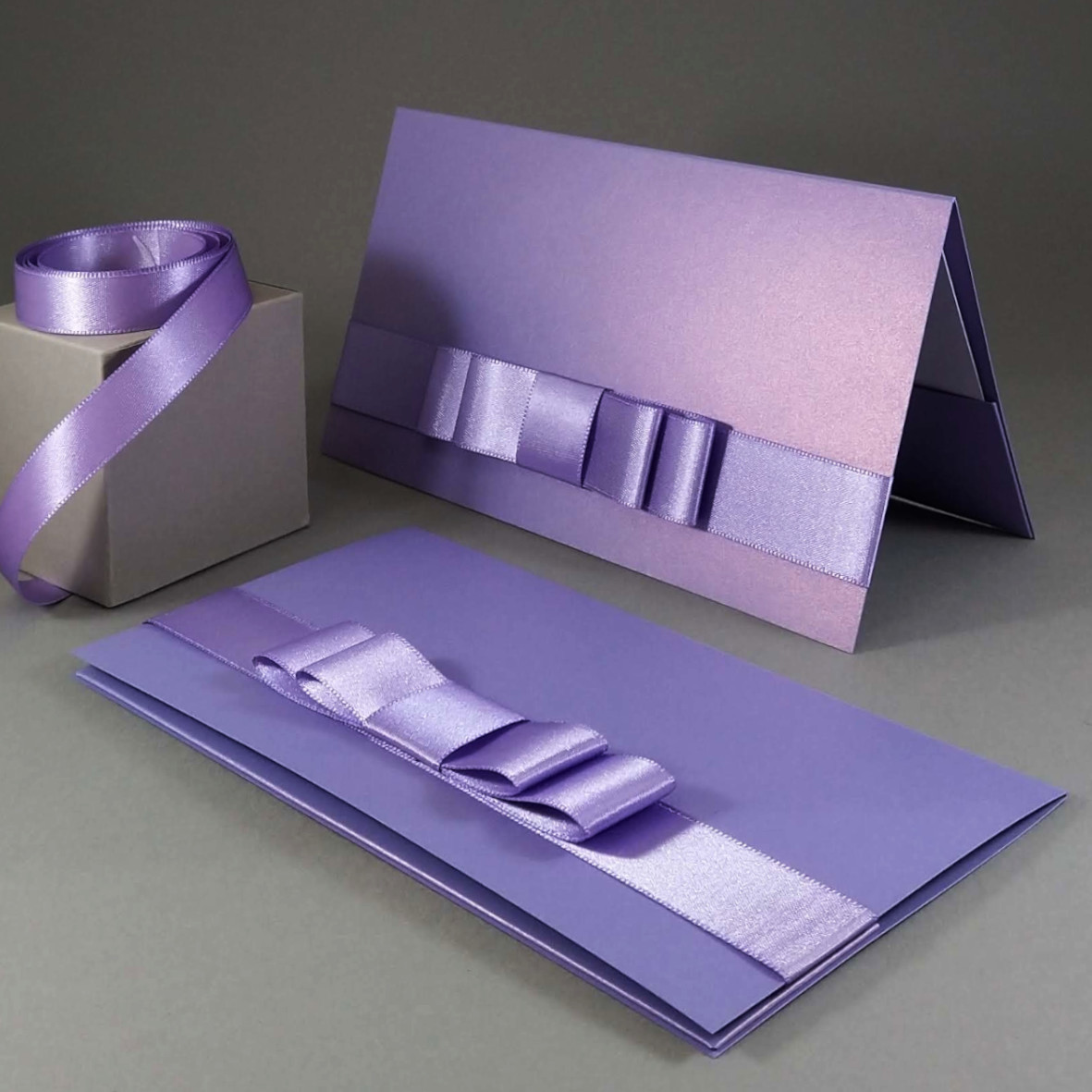 Dárková kapsa DL formátu z perleťového (metalického) papíru, s aplikací z široké atlasové stuhy, vše v fialové barvě, celkový rozměr 206 × 106 mm.