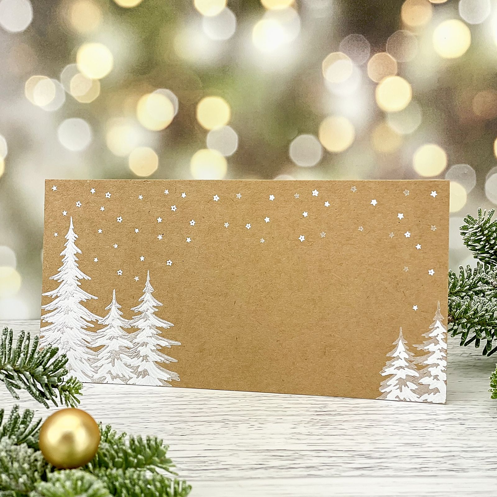 Novoroční–vánoční přání s motivem zasněžených stromů, jednoduchá karta z kraftového papíru, formát 200 × 100.