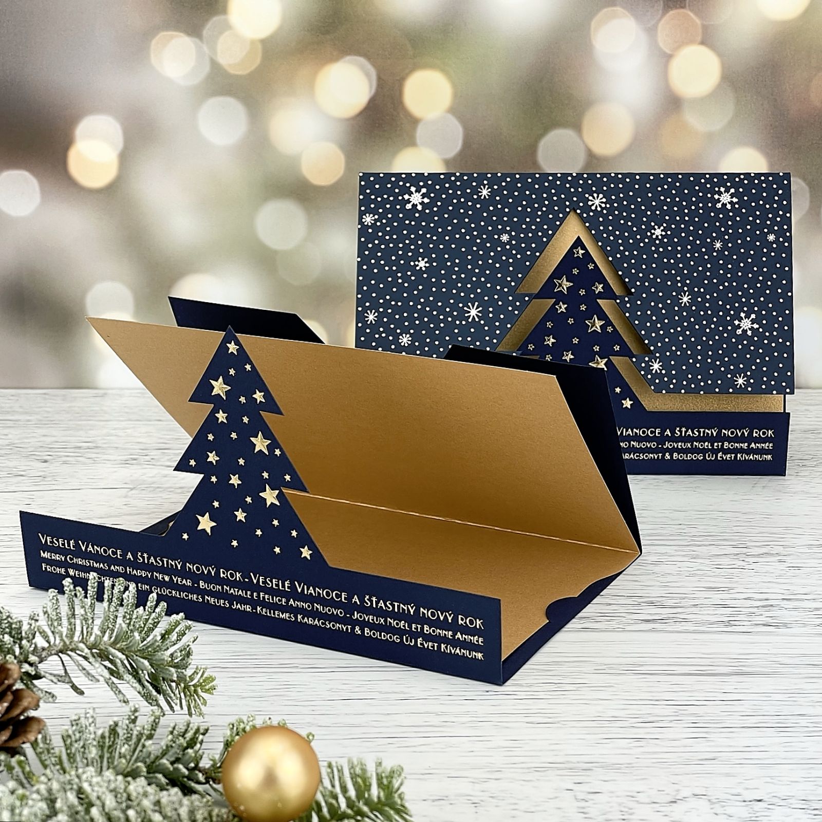 Novoroční–vánoční přání s tvarovým výsekem vánočního stromu a padajícího sněhu, modrý a zlatý grafický papír, otevírací, formát 155 × 110 mm.