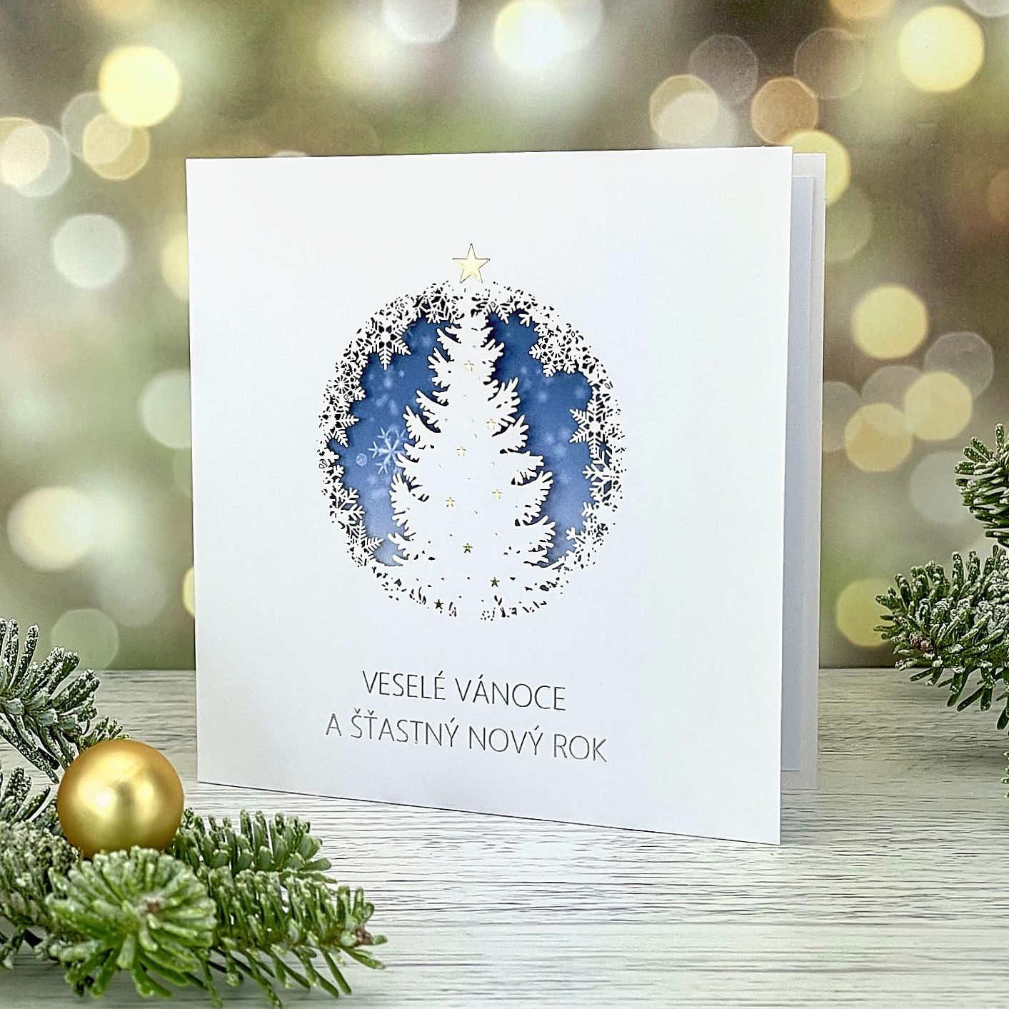 Novoroční–vánoční přání s jemným laserovaným motivem – vánoční strom a vločky, jasně bílý hlazený papír, otevírací, formát 135 × 135 mm.