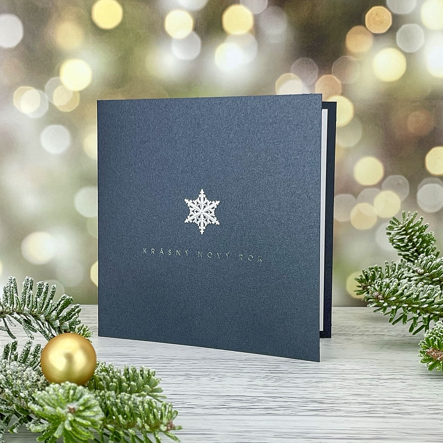 Novoroční–vánoční přání minimalistickým motivem stříbrné vločky, z efektního tmavě šedého perleťového papíru, otevírací, čtvercový formát 135 × 135 mm.