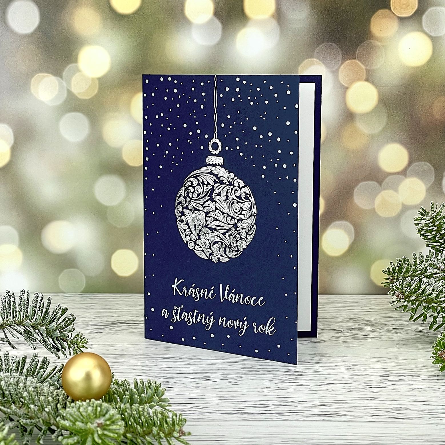 Novoroční–vánoční přání z tmavě modrého grafického papíru, s motivem reliéfní stříbrné baňky a sněhu, otevírací, formát 100 × 150 mm.