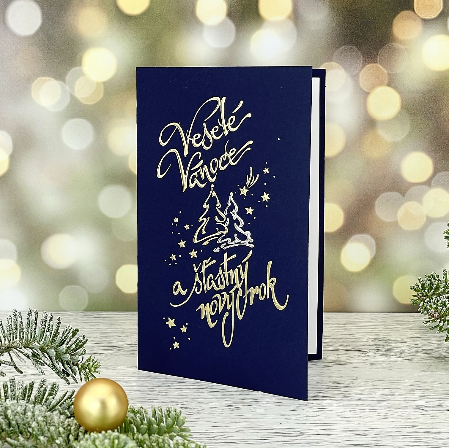 Novoroční–vánoční přání z tmavě modrého grafického papíru, stříbrná a zlatá reliéfní ražba textu, zasněžených stromů, hvězd a komety, přání je otevírací, formát 100 × 150 mm.