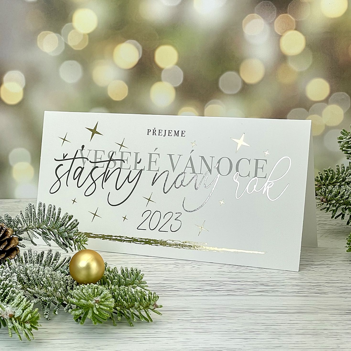Novoroční–vánoční přání z bílého grafického papíru a se zlatou a ocelově šedou ražbou motivu na titulní straně, otevírací, DL formát 200 × 100 mm.