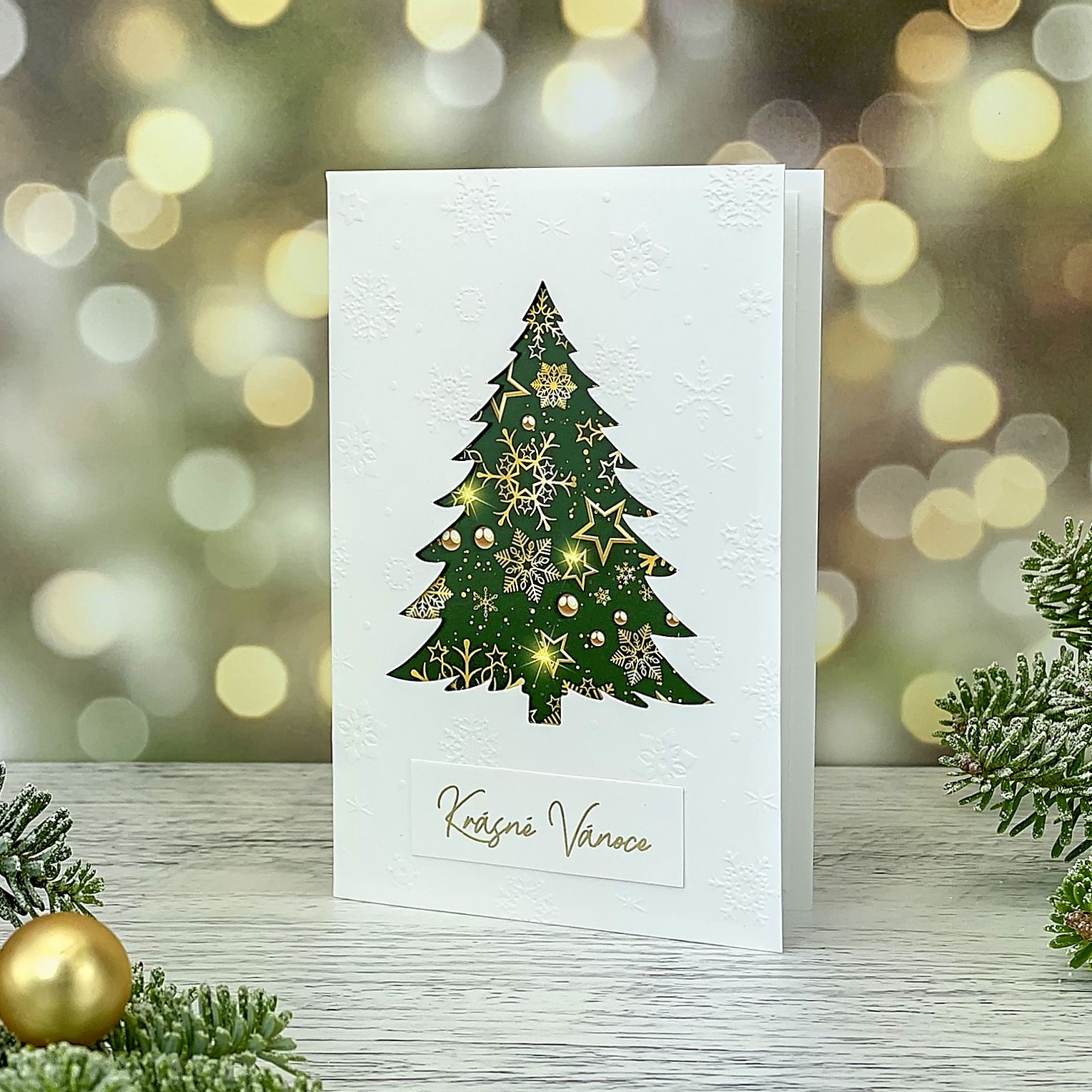 Novoroční–vánoční přání s motivem zeleného vánočního stromu a reliéfních sněhových vloček, bílý grafický papír, otevírací, formát 100 × 150 mm.