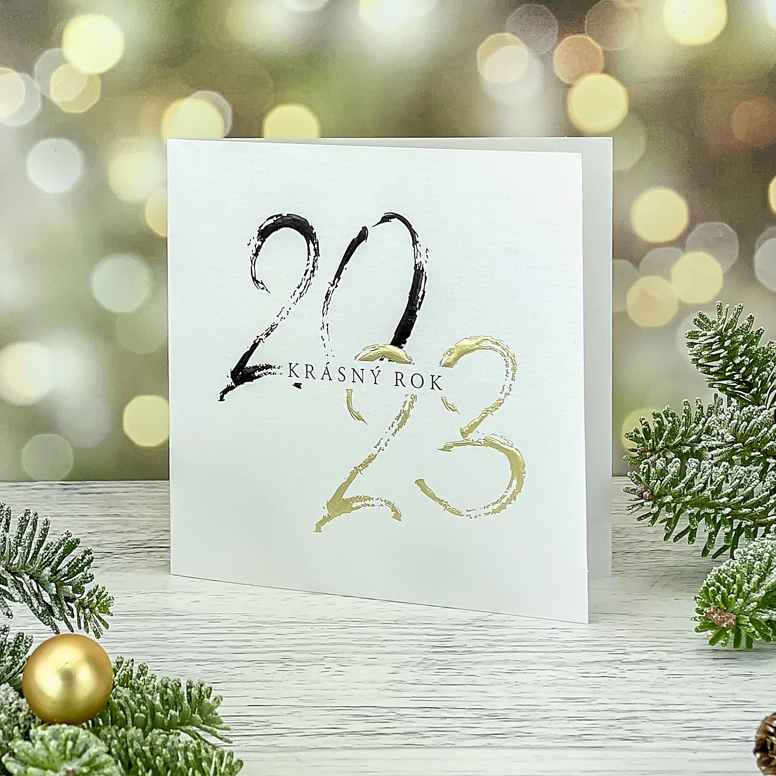Novoroční–vánoční přání s motivem letopočtu na titulní straně provedným zlatou a černou reliéfní ražbou, bílý perleťový papír, otevírací, formát 135 × 135 mm.