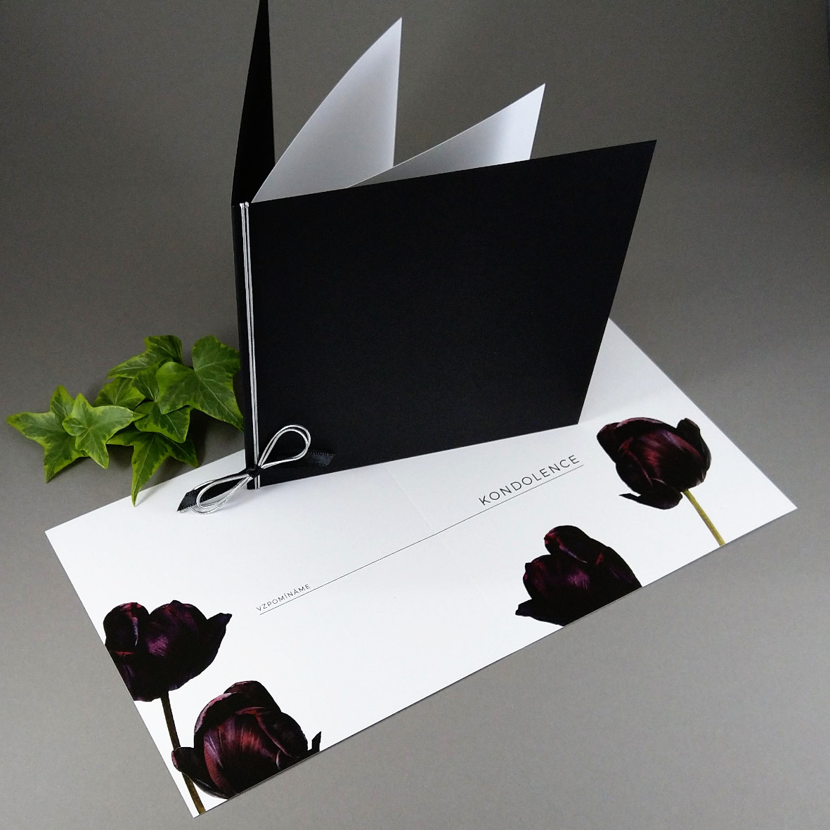 Kondolence s motivem tmavých tulipánů na jasně bílém hlazeném papíru, vložená do černé obálky se stříbrným převazem.