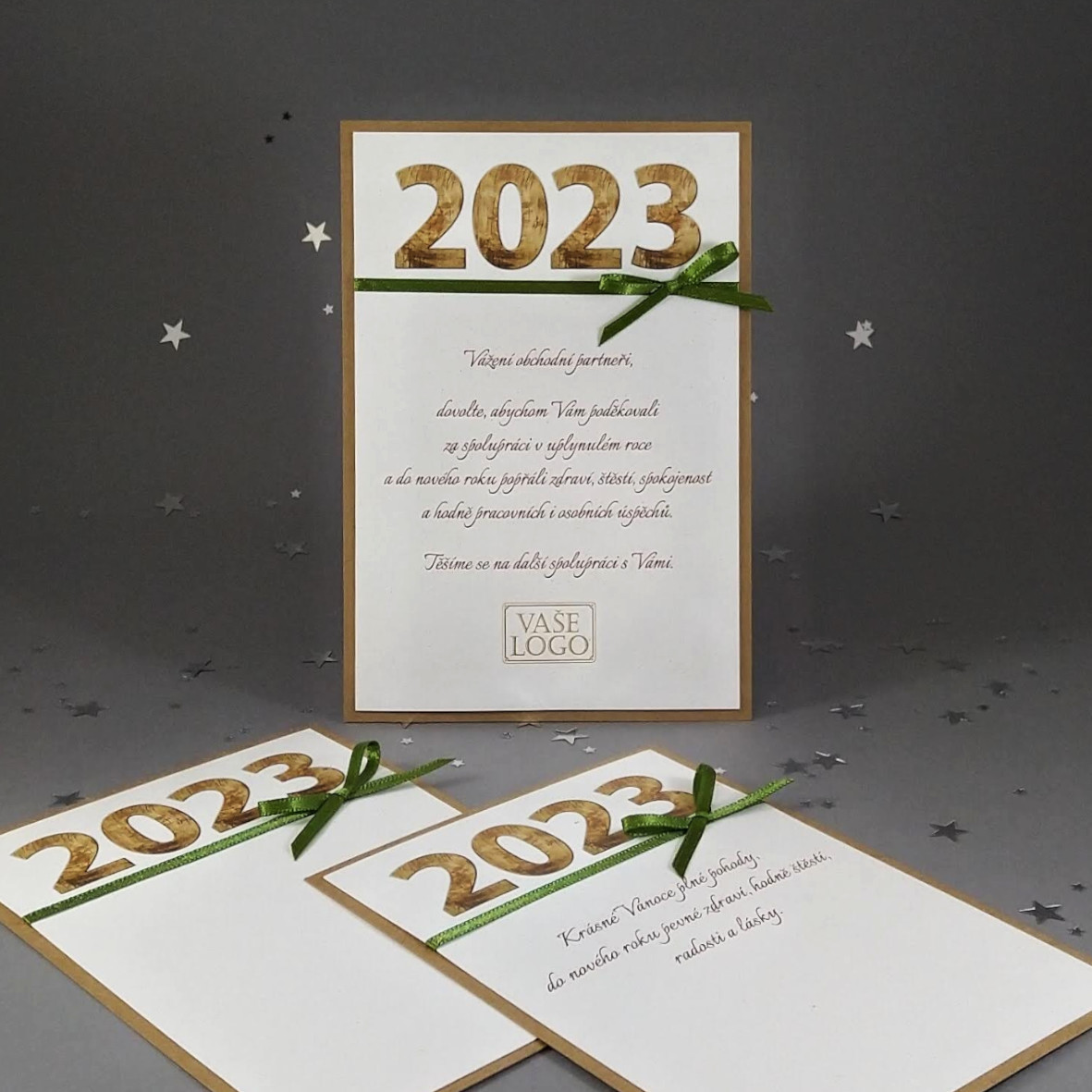 Novoroční přání - dvouvrstvá karta z ekologických recyklovaných papírů s motivem dřevěného letopočtu se zelenou atlasovou stužkou. Formát 110 × 155 mm, digitální tisk.