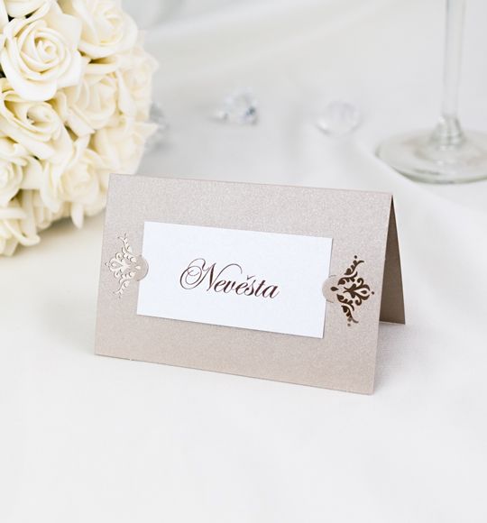 Jmenovka – ze dvou perleťových papírů. Nosná karta s krajkovým motivem svými zámečky upevňuje kartičku s textem, 93 × 60 mm, jednostranná