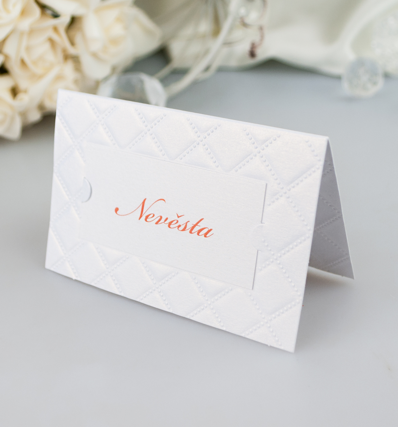 Jmenovka –  v bílé barvě je celoplošně ozdobena slepotiskem. Jméno svatebního hosta je uvedeno na kartičce v zámečcích , 93 × 60 mm, jednostranná