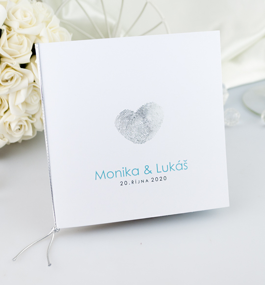 Svatební oznámení v bílé barvě s motivem otisku prstů ve tvaru srdce, převázáno barevným provázkem.